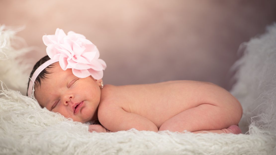 Foto retrato de estudio de Bebe dormida con diadema con flor rosa.